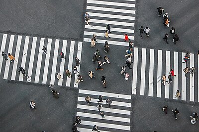 Mehr als die Summe der Teile: Wie Intersektionalität unsere Beziehungen prägt Luftaufnahme einer großen Fußgängerampelkreuzung mit vielen Menschen, die gleichzeitig in verschiedene Richtungen über breite Zebrastreifen gehen.