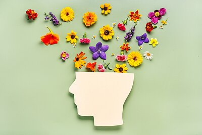 Scherenschnitt eines menschlichen Kopfes, aus dem bunte Blüten kommen, vor einem hellgrünen Hintergrund
